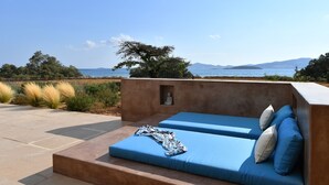 A modern outdoor seating area with blue cushions and a view of the sea.