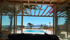 A cozy room with a large sliding glass door leading to a pool area, offering a scenic view of mountains and a tree.