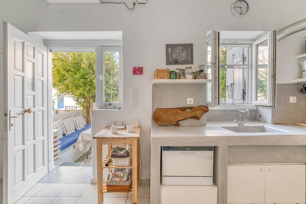 A modern kitchen with a built-in dishwasher, a wooden cutting board, and a window above the sink. - Family House Close to the sea (Paros)