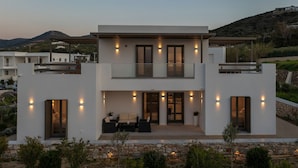 A modern two-story house with a balcony, outdoor seating area, and a stone pathway. - Cozy Haven Studio -island Living Paros- (Paros)