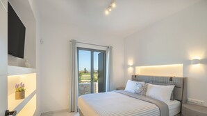 A modern bedroom with a large bed, a TV mounted on the wall, and a sliding glass door leading to a balcony. - Cozy Haven -island Living Paros (Paros)
