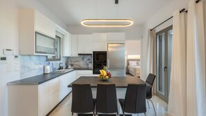 A modern kitchen with white cabinetry, a marble countertop, and a central island with chairs. - Cozy Haven -island Living Paros (Paros)