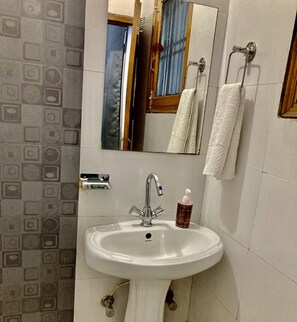 A bathroom with a white sink, a mirror, a towel rack, and patterned tiles on the wall. - The Gleam Hotel (Gurugram)