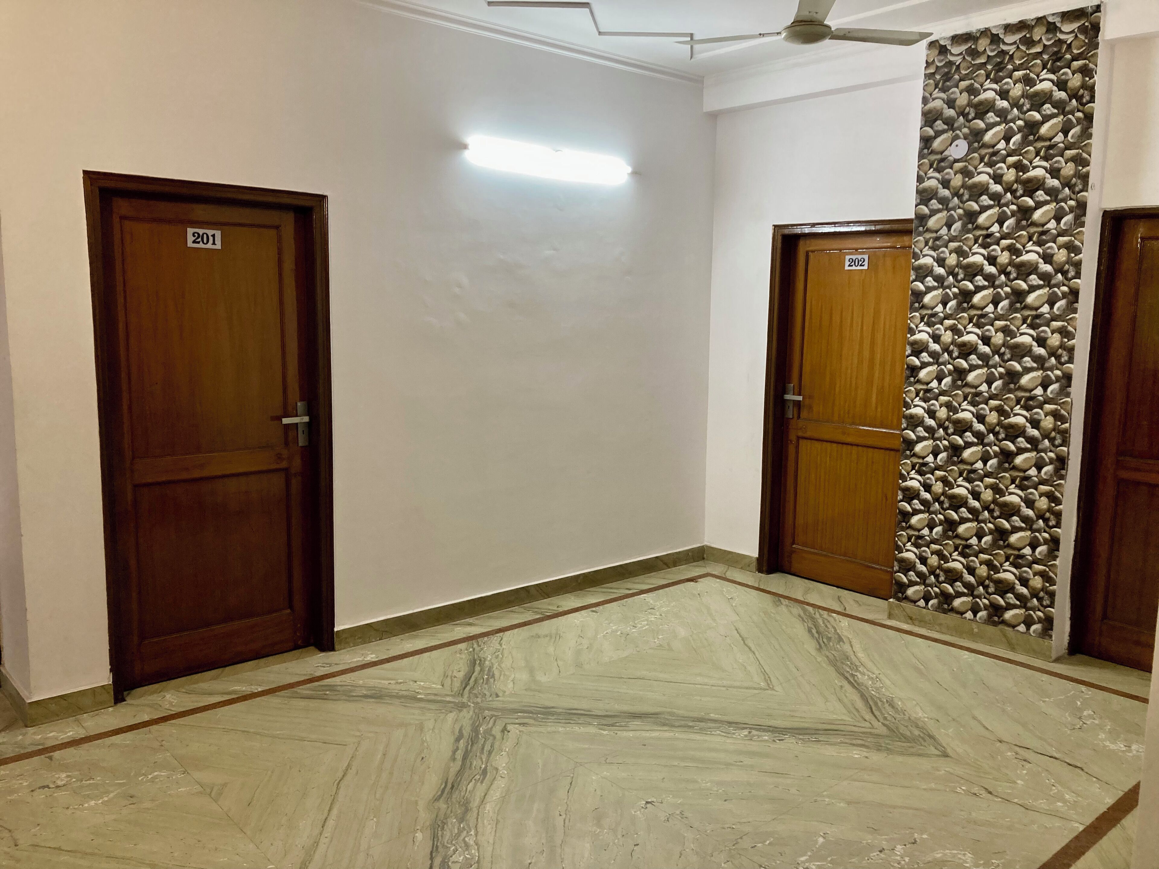 Un pasillo con dos puertas de madera identificadas con los números 201 y 202, un suelo de mármol y una pared con diseño de piedras.