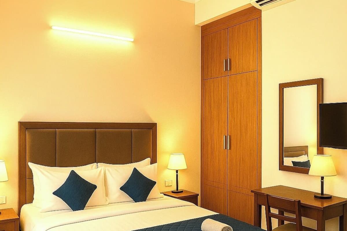 A hotel room with a bed, a desk, a chair, a wardrobe, a ceiling fan, and an air conditioning unit.
