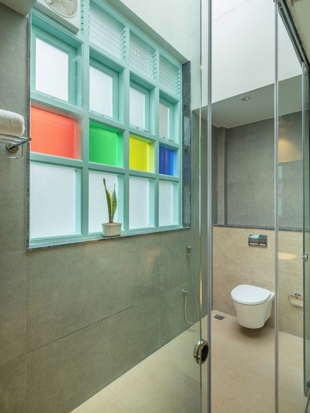 Une salle de bain moderne avec une douche à parois de verre, des toilettes et une fenêtre ornée de panneaux colorés.
