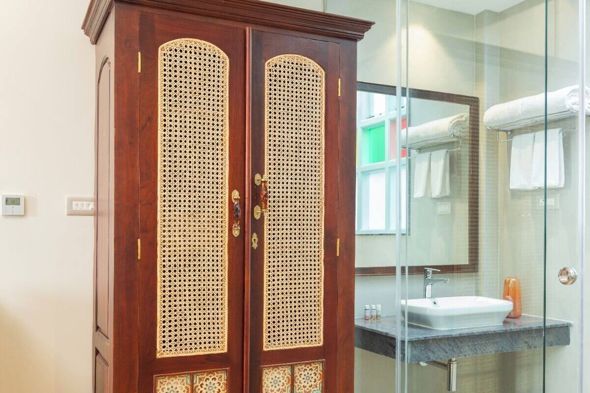 A wooden wardrobe with intricate designs, a glass shower enclosure, and a bathroom with a sink and towel rack.