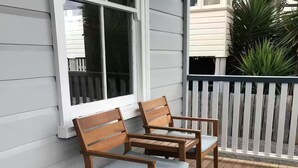 A wooden deck with two chairs and a table, a white railing, and a window with blinds. - Eton Cottage: Central Boutique Stay (East Toowoomba)