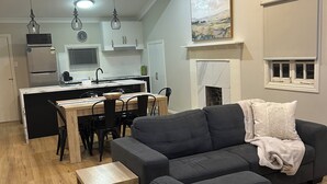A modern living room with a dark grey sectional sofa, a wooden coffee table, and a fireplace. - Eton Cottage: Central Boutique Stay (East Toowoomba)