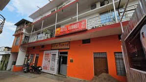A two-story building with a prominent orange facade, a sign for 'Hotel Sunset' indicating it is a backpackers hostel, and a visible entrance with a metal gate. - Hotel Sunset Orchha (Orchha)