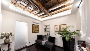 Una sala de estar moderna con suelo de madera oscura, un sofá gris, una planta grande en maceta y un tragaluz con vigas de madera a la vista.