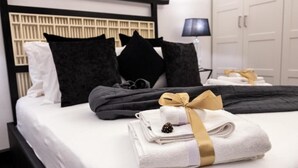 Una cama bien hecha con ropa de cama blanca y negra, un cabecero negro y una pila de toallas dobladas con una cinta dorada.