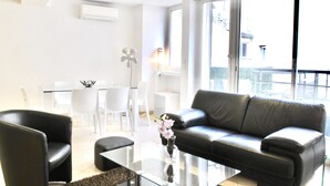 Un saló modern amb un sofà de cuir negre, una taula de centre de vidre i una taula de menjador blanca amb cadiretes.