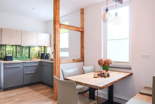 A modern kitchen with grey cabinets, a wooden dining table, and a window with a view of greenery.
