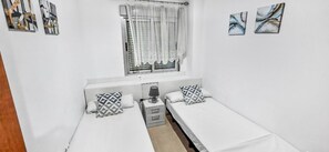 A small, clean room with two single beds, a window with curtains, and a bedside table with a lamp.