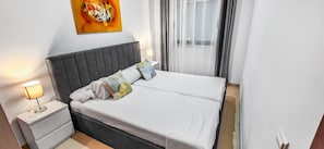 Een net opgemaakt bed met witte lakens en een grijs hoofdbord, een bedlamp en een wanddecoratie met abstracte kunst.