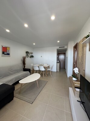 A modern living room with a sofa, a coffee table, a dining table with chairs, a TV, and a small plant.