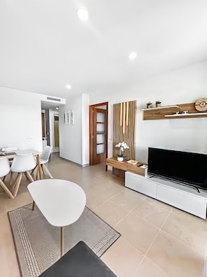 Een moderne woonkamer met een flatscreen televisie, een eethoek met stoelen en een wand met houten accenten.