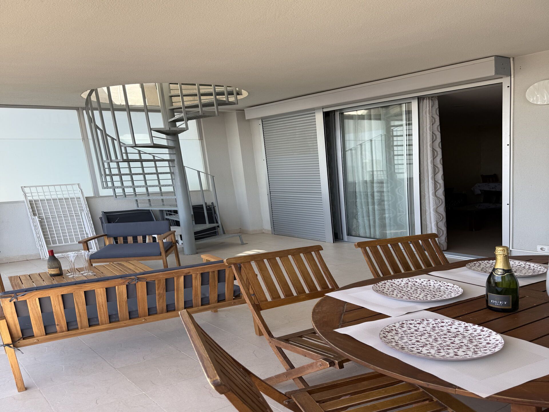 En balkon med en spiraltrappe, træmøbler og et bord dækket til spisning.