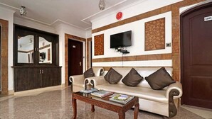 Un vestíbulo con sofá, una mesa de centro, un televisor montado en la pared y una puerta con placa de número.