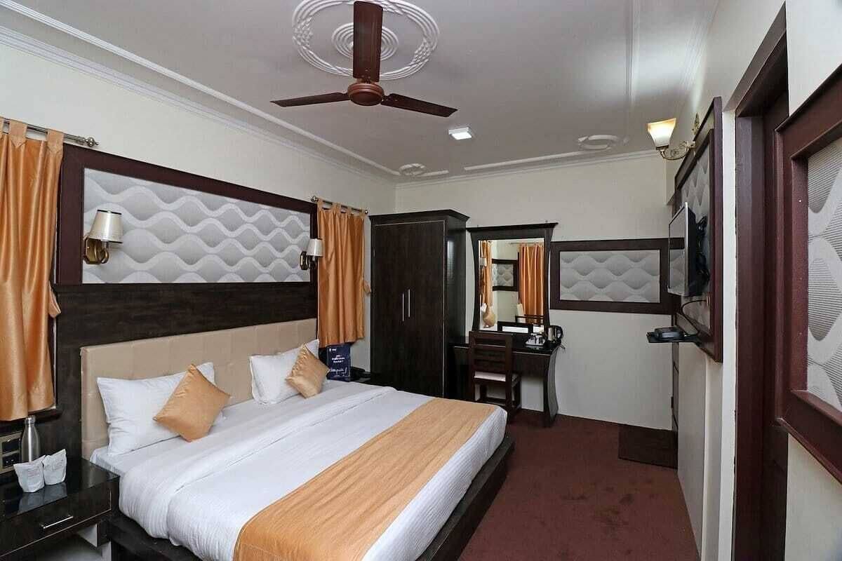 A hotel room with a large bed, a desk, a chair, a wardrobe, a mirror, and a ceiling fan.