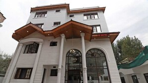 Un hotel con fachada blanca, múltiples ventanas y una entrada central con un toldo de madera.
