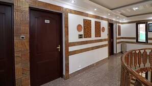 Un pasillo con una puerta de madera que indica “2002”, una pared con paneles decorativos y una escalera con barandillas ornamentales.