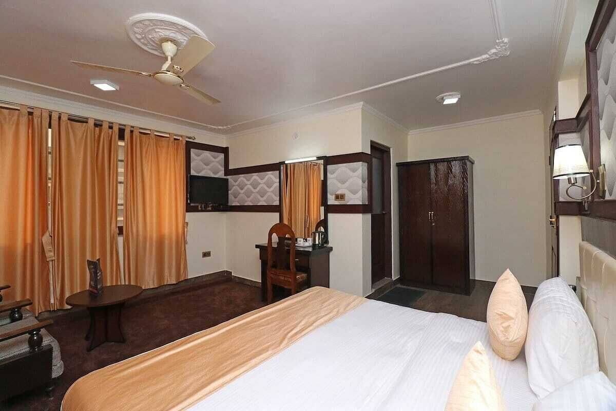A hotel room with a bed, a desk, a chair, a wardrobe, and a ceiling fan.