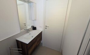 Ett modernt badrum med ett vitt handfat, ett mörkt träfärgat tvättställ och en stor spegel.