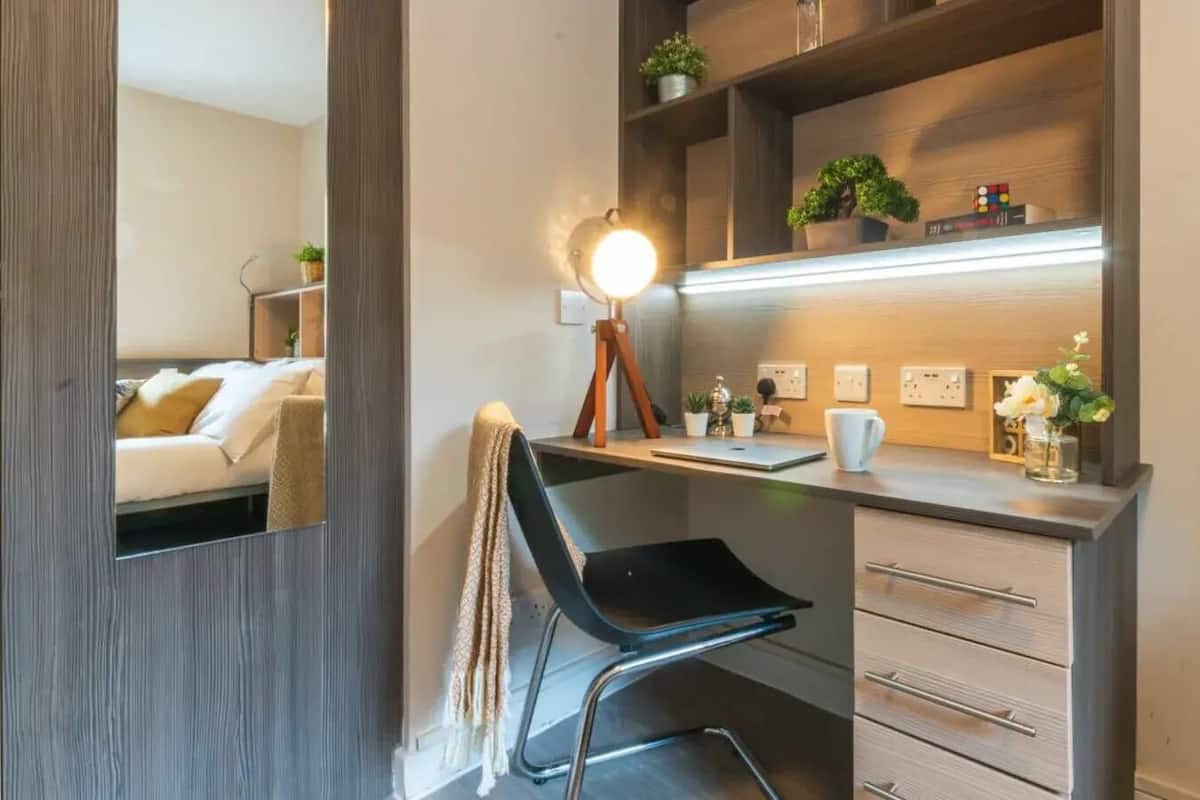 A modern bedroom with a bed, a chair, a desk, and a mirror.