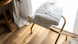 A wooden chair with a white towel draped over it, positioned near a window with sheer curtains.