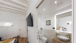 A modern bathroom with a wooden floor, a white vanity with a large sink, a toilet, and a shower area.