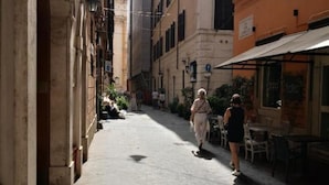 A narrow street with buildings on either side, outdoor seating, and a few pedestrians. - Barcaccia Luxury Suites: Executive Suite 2 (Roma)