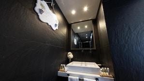 A modern bathroom with a dark stone wall, a white sink, and a mirror above it. - Barcaccia Luxury Suites: Executive Suite 2 (Roma)