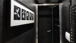A modern bathroom with a black tiled wall, a framed picture of flowers, and a glass shower enclosure. - Barcaccia Luxury Suites: Executive Suite 2 (Roma)