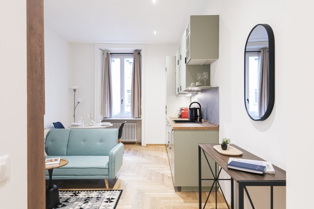 Un espace de vie compact comprenant un coin cuisine, un canapé, une petite table et un miroir.