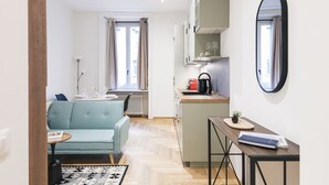Un espacio habitable compacto con kitchenette, un sofá, una mesa pequeña y un espejo.