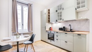 Una cocina moderna con comedor, con armarios de colores claros, horno empotrado y cafetera.