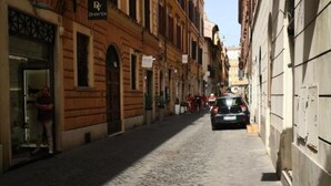 A cobblestone street lined with historic buildings, a parked car, and a person walking. - Barcaccia Luxury Suites: Suite Queen 3 (Roma)