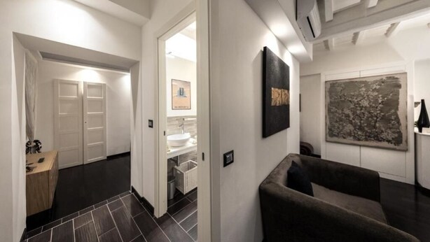 A modern interior with a dark tiled floor, a sofa, a painting, and a bathroom visible through an open door. - Barcaccia Luxury Suites: Suite Queen 3 (Roma)