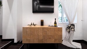 A modern room with a wooden console table, a flat-screen TV mounted above it, and a window with sheer curtains. - Barcaccia Luxury Suites: Suite Queen 3 (Roma)