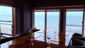 Zona de dinar amb vista a l'oceà, que inclou una taula de fusta, cadires i copes de vi.