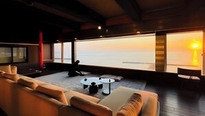 Un interior modern amb un sofà, una taula rodona petita i vista al mar al capvespre.