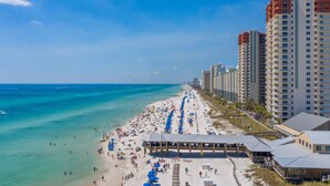 A beach with a long stretch of umbrellas and beach chairs, adjacent to tall residential buildings.