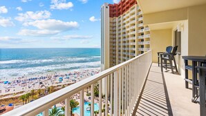A balcony with a view of the beach and ocean, a pool, and outdoor seating.