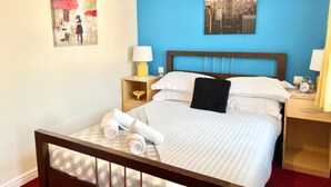 A hotel room with a bed, two bedside tables, a nightstand, a blue wall, and two paintings. - Quiet 2bedroom Home-garden-parking-family Friendly (Swansea)