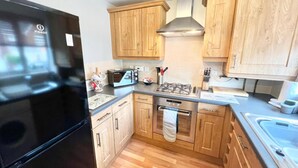 A compact kitchen with wooden cabinets, a stainless steel range hood, a microwave, and a refrigerator. - Quiet 2bedroom Home-garden-parking-family Friendly (Swansea)