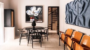 Een eethoek met een ronde tafel en stoelen, een bloemschilderij aan de muur en een trap op de achtergrond.