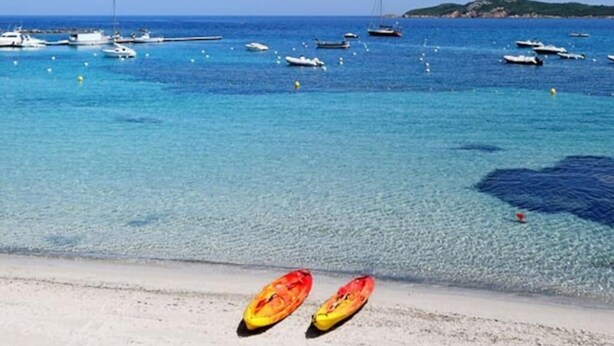 A beach with clear blue water, boats, and a small hill in the distance.