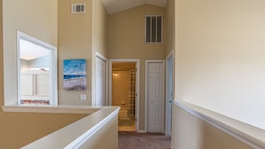 A hallway with beige walls, white trim, a painting, and a door leading to a bathroom.